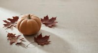 Orange pumpkin with autumn maple leaves on neutral linen fabric background. Seasonal fall harvest decoration for thanksgiving holiday celebrations.