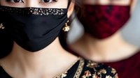 Young woman wearing black protective face mask decorated with rhinestones and crystals, matching elegant evening dress. Fashion during pandemic concept.