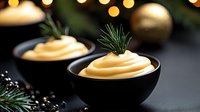 Creamy holiday appetizer in elegant black bowls garnished with fresh rosemary sprigs against festive Christmas background with golden ornaments and pine branches.