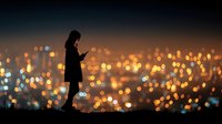 Young woman silhouette using smartphone against blurred city lights at dusk. Urban lifestyle and mobile technology concept for social media designs.
