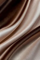 Smooth flowing folds of luxurious brown and beige satin fabric create elegant waves and curves with soft shadows and highlights for fashion and luxury backgrounds.