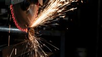 Industrial worker using angle grinder creating bright sparks in metalworking shop. Safety equipment and protective gear for manufacturing processes.