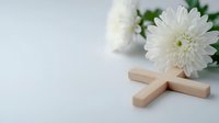 Wooden cross and white chrysanthemum flower on light background, symbolizing faith, remembrance and spiritual peace. Religious funeral concept.