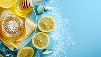 Fresh honey jar with lemon slices, mint leaves and scattered sugar on turquoise blue background, top view composition for natural remedy and tea concept.