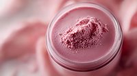Pink mineral powder makeup in round transparent jar, soft focus cosmetic photography on blush pink background with selective depth of field.