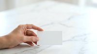 Woman's hand holding blank white business card on marble surface for branding and corporate identity mockup presentations.