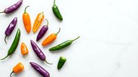 Colorful hot chili peppers scattered on white marble background. Fresh spicy vegetables for cooking, seasoning and culinary ingredients in kitchen.