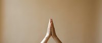 Hands pressed together in prayer or namaste gesture against a warm beige background, symbolizing mindfulness, gratitude, and spiritual practice.