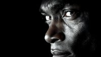 Side profile portrait of African American person against black background with dramatic lighting highlighting facial features and intense gaze in monochromatic style.