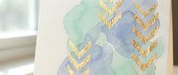 Abstract watercolor background with gold foil chevron arrows in mint green and lavender purple hues for modern design projects and stationery.