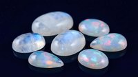 Collection of polished opal gemstones displaying rainbow fire and iridescent colors on dark background for jewelry making and luxury accessories.