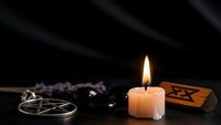 Burning candle with occult symbols, pentagram and mystical objects on dark background for spiritual rituals and esoteric practices.