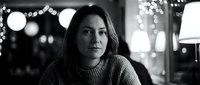 Young Asian woman in cozy sweater sitting thoughtfully in cafe with warm bokeh lights creating intimate atmospheric mood for lifestyle content.