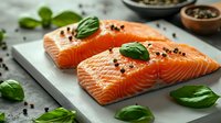 Fresh raw salmon fillets garnished with basil leaves and black peppercorns on gray stone background, healthy omega-3 rich seafood for cooking.