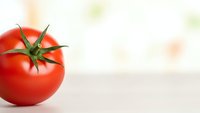 Fresh red tomato with green stem on white surface with soft bokeh background for healthy cooking and nutrition concepts.