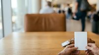 Closeup of hands holding blank white card at wooden table with brown leather chair and blurred office background, suitable for business mockups and corporate presentations.