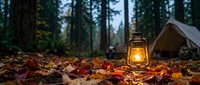 Vintage lantern glowing warmly among colorful autumn leaves at forest campsite with tent in background during twilight camping adventure.
