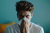 Young Caucasian male blowing nose into tissue against turquoise background, showing symptoms of seasonal allergy, cold or flu. Perfect for health and medical advertising.