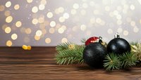 Festive Christmas decoration with black and red ornaments on pine branches against wooden surface with golden bokeh lights in background.