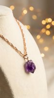 Amethyst crystal pendant on rose gold chain displayed on cream fabric form with warm bokeh lights, suitable for jewelry marketing and e-commerce.
