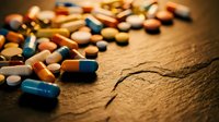 Colorful pharmaceutical pills and capsules scattered on wooden surface with visible crack, representing medicine, healthcare and treatment options.