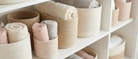 Organized bathroom linen storage with rolled towels in woven baskets on white shelves. Home organization and spa-like bathroom decor concept.
