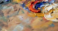 Artist palette with vibrant oil paints mixed in red, blue, yellow and orange colors on wooden surface for creative painting and art projects.
