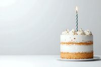 Mini layered vanilla cake with whipped cream frosting and single lit striped candle on white plate against light gray background, minimalist celebration setup.