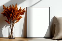 Minimalist mockup with empty black frame, dried orange pampas grass in glass vase on wooden surface against white wall with natural shadows.
