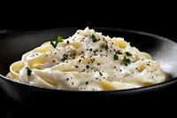 Creamy fettuccine pasta with white sauce garnished with black pepper and fresh parsley served in dark plate on black background, dramatic food photography.