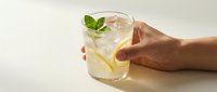 Refreshing lemonade with mint garnish held by hand on neutral background for beverage marketing and summer drink promotions.