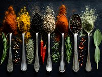 Colorful spices and herbs arranged on vintage spoons against dark background, with peppercorns, chili, rosemary and bay leaves for cooking.