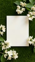Blank white paper card surrounded by delicate white jasmine flowers on green grass background for spring wedding invitations and greeting cards.