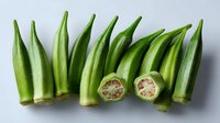 Fresh green okra pods arranged in row with two cross sections showing internal star pattern and seeds on white background, isolated for food photography.
