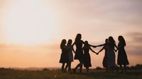 Group of women holding hands in circle dancing together at sunset in field creating silhouettes against golden sky for friendship and unity concepts.