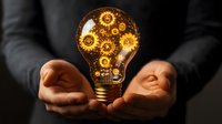 Glowing lightbulb with golden mechanical gears inside held in cupped hands against dark background, representing innovation and creative business solutions.