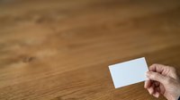Hand holding blank white business card on wooden surface for branding and corporate identity design projects.