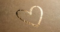 Heart shape drawn in wet sand on beach shore with gentle waves and natural lighting for romantic vacation concepts.