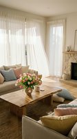 Cozy living room interior with soft natural light, white curtains, beige sofa, wooden coffee table, pink tulips, stone fireplace for home decor inspiration.