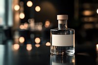 Clear glass bottle with blank label on dark reflective surface against blurred bokeh lights background, creating luxurious atmosphere for premium product photography.