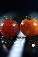 Fresh cherry tomatoes with water drops on dark background, dramatic lighting creates artistic food composition with bokeh effect and reflective surface.