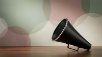 Vintage black megaphone resting on a wooden surface against a soft pastel bokeh background, evoking retro communication and announcement concepts.