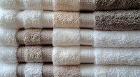Stack of fresh white and beige cotton bath towels neatly folded and arranged in rows, showing soft texture and stripes pattern for spa, hotel or home decor.