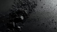 Dark textured surface with scattered powder and granular particles creating dramatic shadows and highlights against black background, macro photography for cosmetic products.