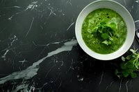 Fresh green vegetable soup with herbs in white bowl on black marble background, top view. Healthy detox spring meal for restaurant menu and food blogs.