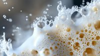 Macro shot of beer foam with rising bubbles and golden droplets creating dynamic texture against dark background, capturing effervescent beverage detail.