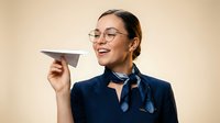 Young woman with East Asian ethnicity, wearing round eyeglasses and dark blue shirt, holding paper airplane, smiling against beige background. Suitable for business, creativity, innovation, startup concepts.