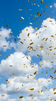 Golden confetti pieces falling through bright blue sky with white fluffy clouds creating festive celebration atmosphere for party and success concepts.