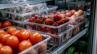 Fresh ripe strawberries and tomatoes in plastic containers on grocery store shelf, retail produce display with bright natural colors and selective focus.
