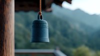 Traditional bronze temple bell hanging from rope against blurred mountain landscape background, creating peaceful zen atmosphere for meditation and spiritual practices.